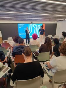 Carolina Martinez, diretora-geral da Stanford Social Innovation Review Brasil, e Gelson Henrique, diretor-executivo da Iniciativa PIPA, discursam em um palco diante de algumas pessoas no lançamento do podcast PSIR!