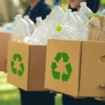 foto de três pessoas segurando caixas com símbolos de reciclagem estampados e garrafas plásticas dentro