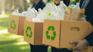 foto de três pessoas segurando caixas com símbolos de reciclagem estampados e garrafas plásticas dentro