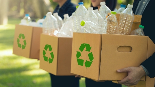 foto de três pessoas segurando caixas com símbolos de reciclagem estampados e garrafas plásticas dentro