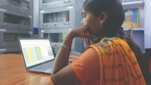 Foto de uma jovem usando roupa tradicional indiana na cor laranja, sentada em um escritório enquanto mexe no computador